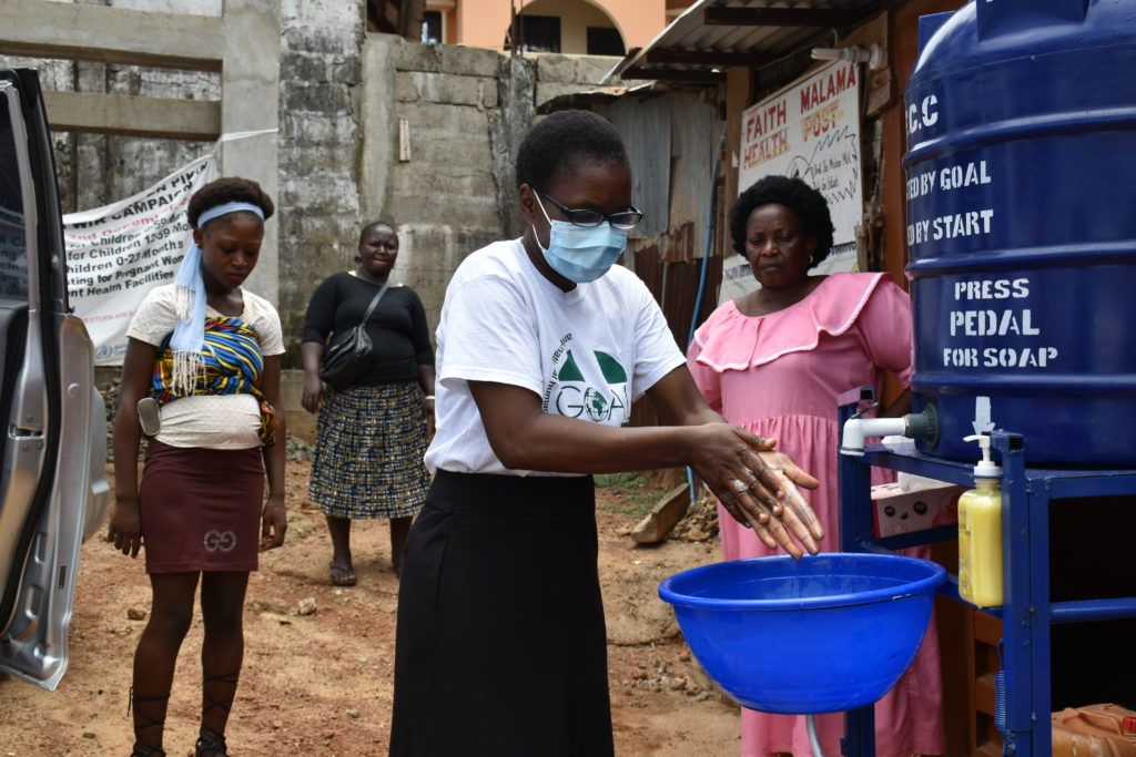 GOAL staff member Mariama demonstrates the handwashing method while wearing a face mask in Freetown. 
