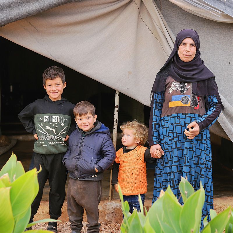 Photograph of Syrian grandmother and her three young grandchildren outside their tent at a displacement camp in Kelly, Syria.