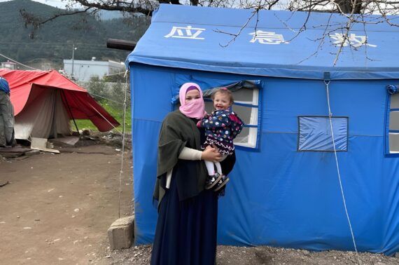 Syrian women stands in refugee camp in Türkiye with child