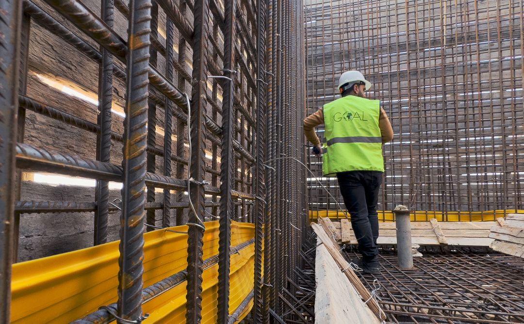 A man wearing a high visibility vest with the GOAL logo on the back surveying a water tower that is being constructed in Idleb, Northwest Syria