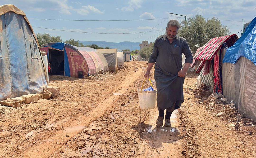 A man carrying a bucket of water bought from private vendor to bring back to the tent he shares with his family at a displacement camp in Aleppo, Northwest Syria.