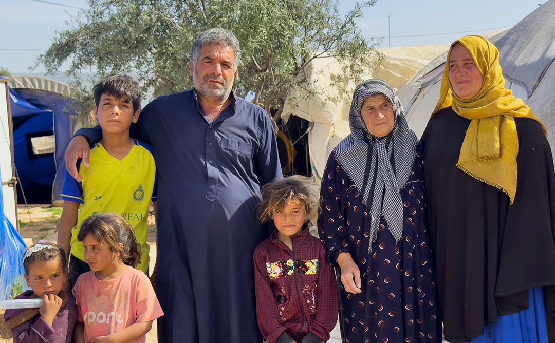 Three generations of a Syrian family standing outside a tent that they've been living in since the February 2023 earthquakes destroyed their home