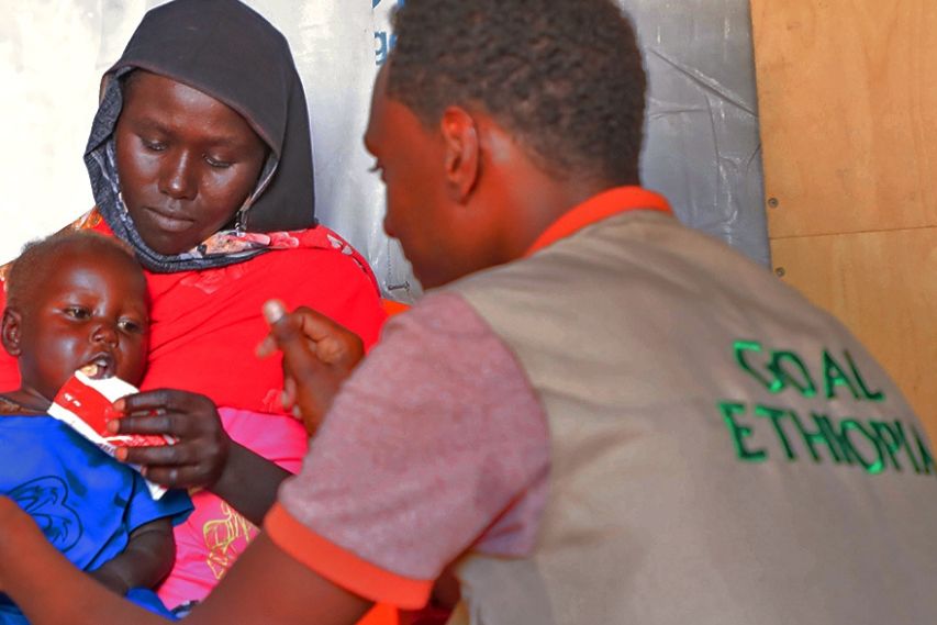 GOAL RG ACQ Campaign_Malnutrition_Ethiopia_GOALie A mother feeding her child nutritional peanut paste to help fight malnutrition while a GOAL Ethiopia staff is helping on her right