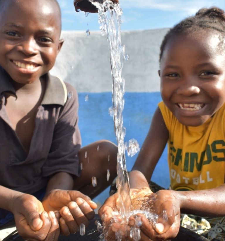 GOAL RG ACQ Campaign_Water (1) Two children in Sierra Leone smiling and happy as they hold their hands under clean running water