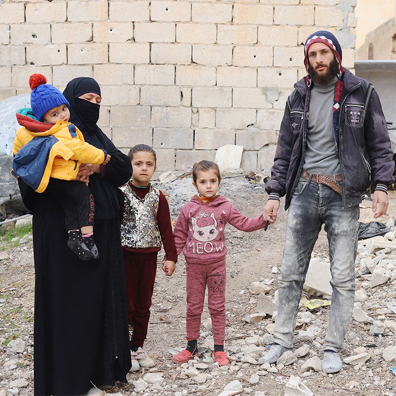 SANAD Cycle 2_SY_Amina Family_Sarmin_body_Square A family in Syria standing in front of the rubbles of their village left from the nearly 14-year-old war