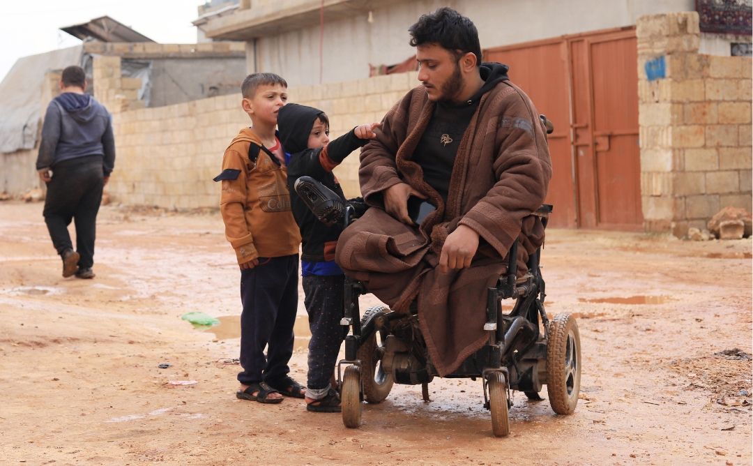 SANAD Cycle 3_LP_Body Image Abu Ahmel with two of his children, Rami (6) and Fadi (3), in their camp in the outskirts of Kelly, northwest Syria. Accessibility is one of the many challenges that people with disability face in displacement camps.
