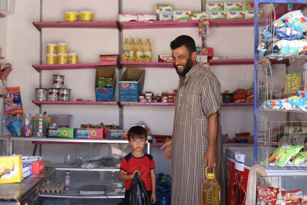 Ahmed Al-Ibrahim, 45 years old, buys food at the market with his 4-year-old son Omar in Haysh after receiving GOAL's cash assistance.