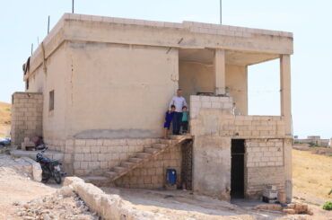 A man and his two children standing outside their home in Kafr Sajnah, Idleb.