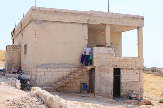 A man and his two children standing outside their home in Kafr Sajnah, Idleb.